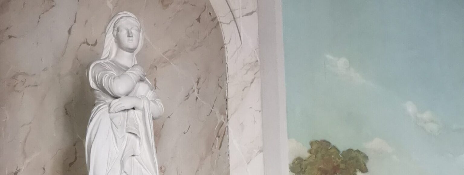 Weiße Frauenstatue in einer marmorierten Wandnische neben einem Wandgemälde mit Wolkenhimmel.