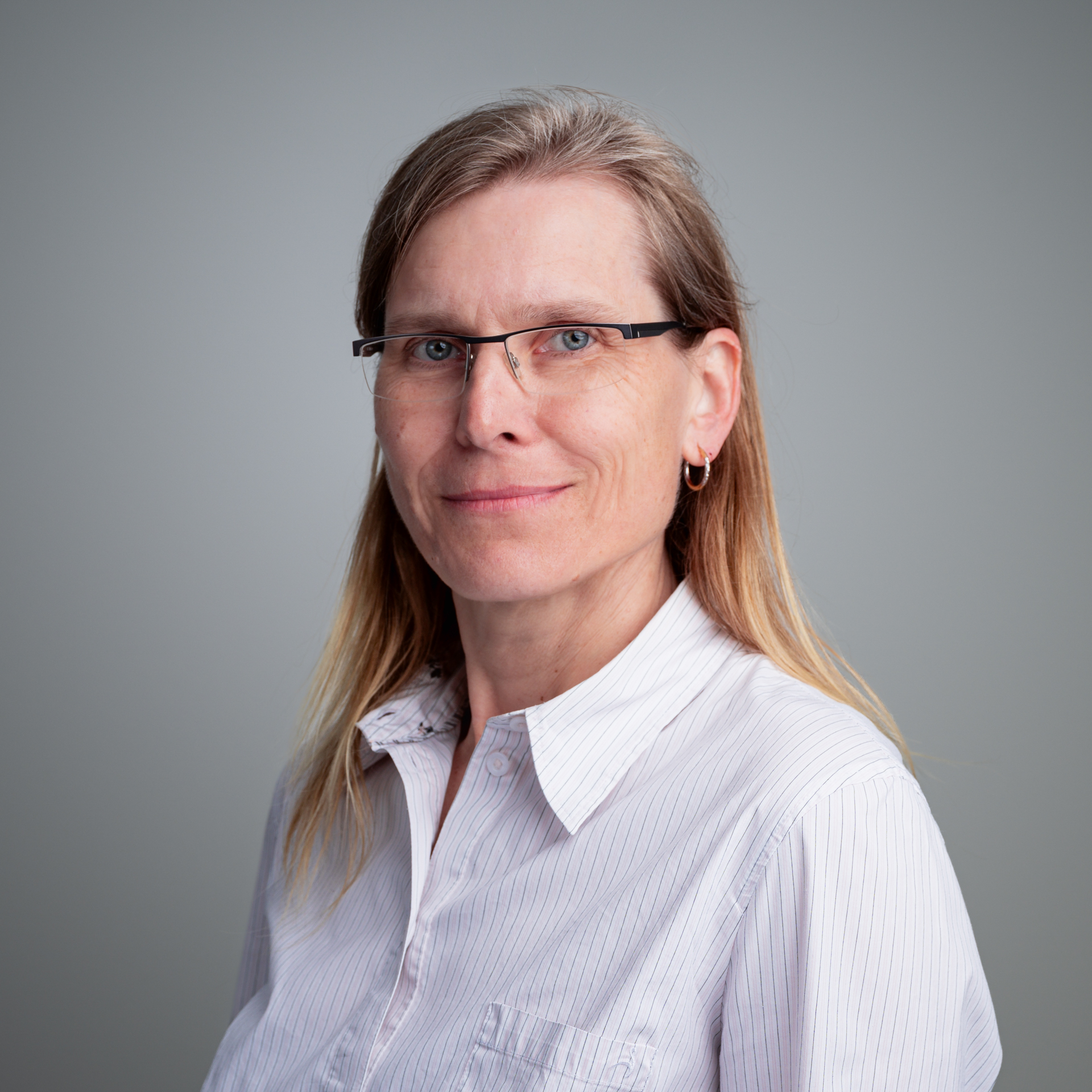 Porträt von Mareike Lemster, einer Frau mit blonden Haaren, Brille und einem gestreiften Hemd, die leicht lächelt.