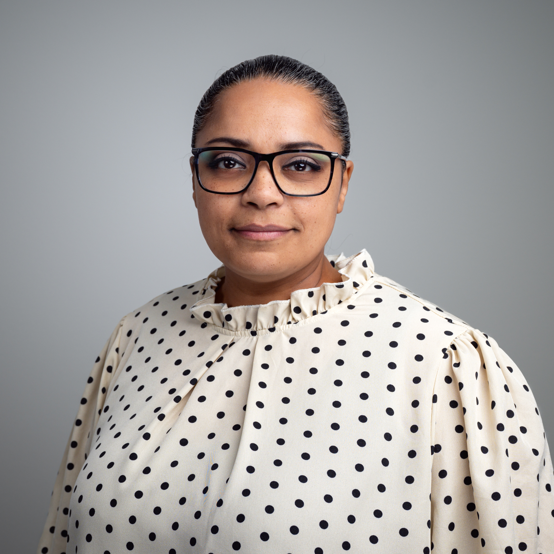 Porträt von Petra Sailer, einer Frau mit dunklen Haaren, Brille und einer gepunkteten Bluse, die direkt in die Kamera blickt.