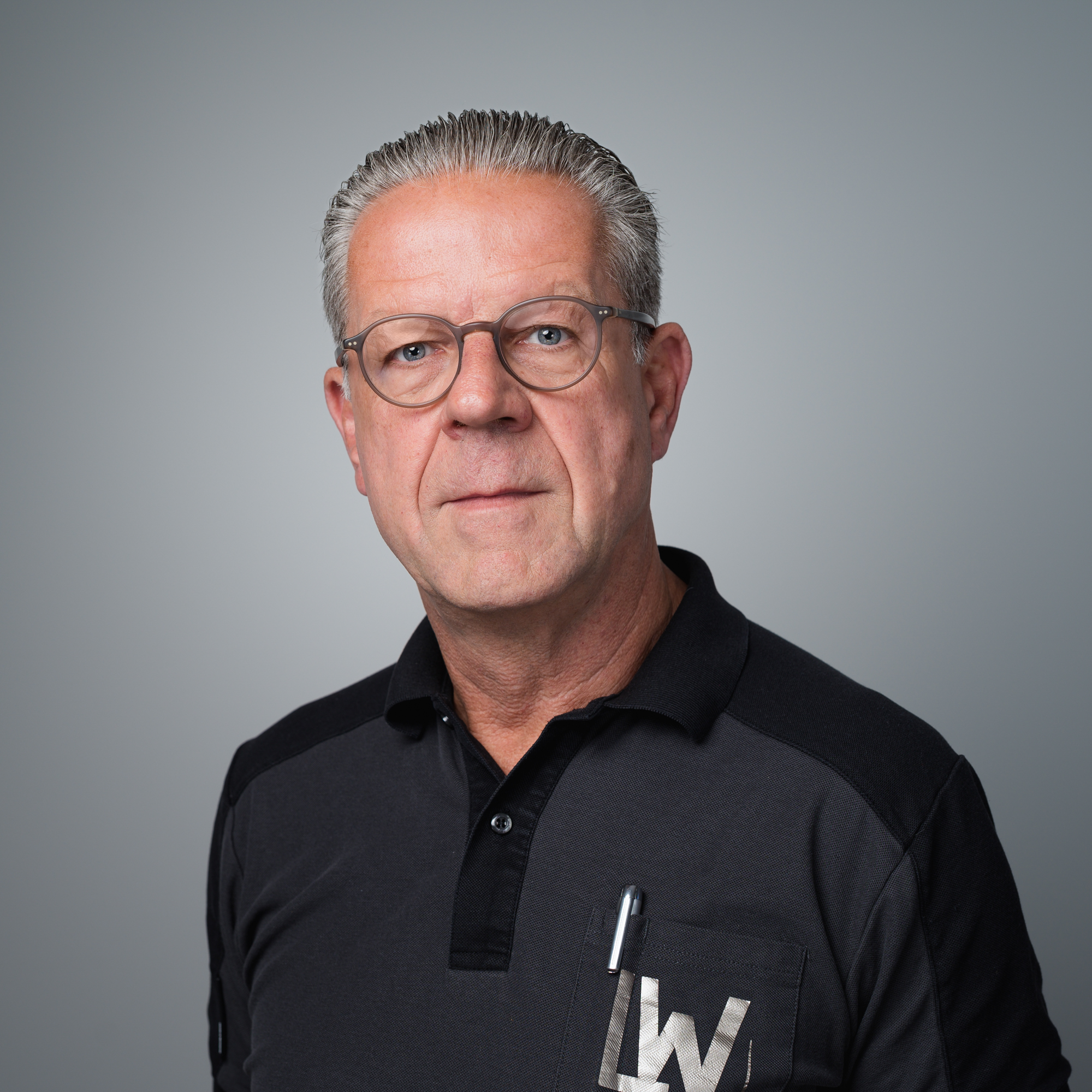 Porträt von Andreas Jurgeleit, einem Mann mit grauen Haaren und Brille, der ein dunkles Poloshirt trägt und direkt in die Kamera blickt.