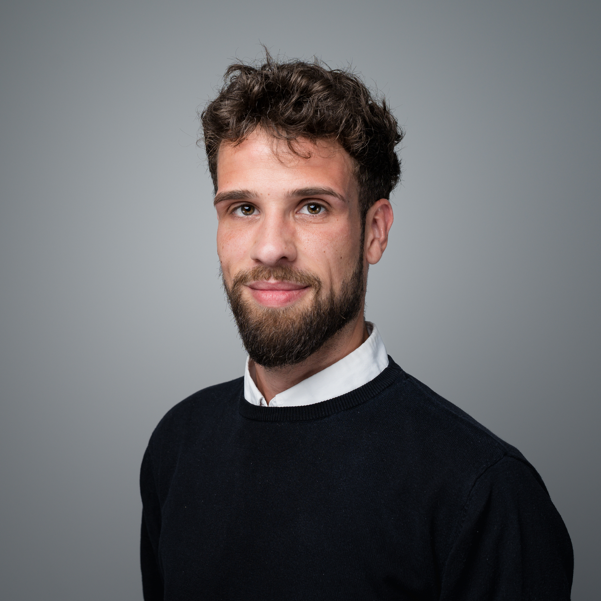 Porträt von Dennis Schunowski, einem jungen Mann mit lockigem Haar und Bart, der in die Kamera blickt und leicht lächelt.