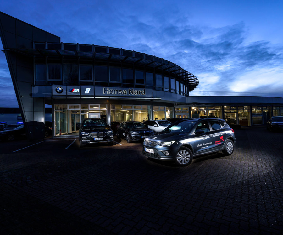 Ein modernes Autohaus 'Hansa Nord' bei Nacht, mit einem beleuchteten Fahrzeug des Lübecker Wachunternehmens im Vordergrund.
