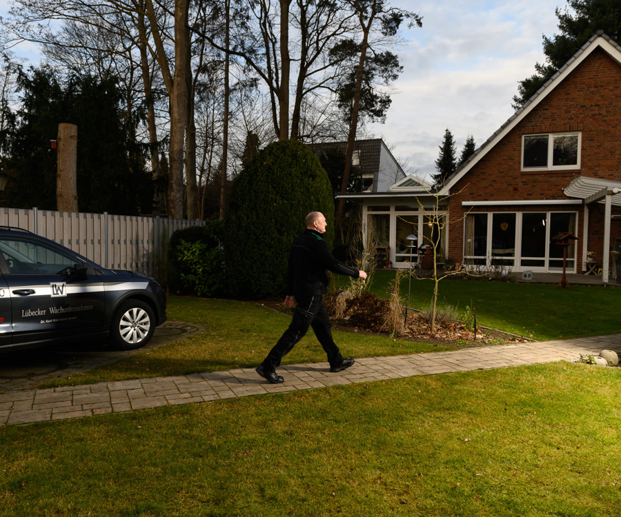 Ein Mitarbeiter des Lübecker Wachunternehmens geht auf Funkstreife an einem Firmenwagen und einem Wohnhaus vorbei.