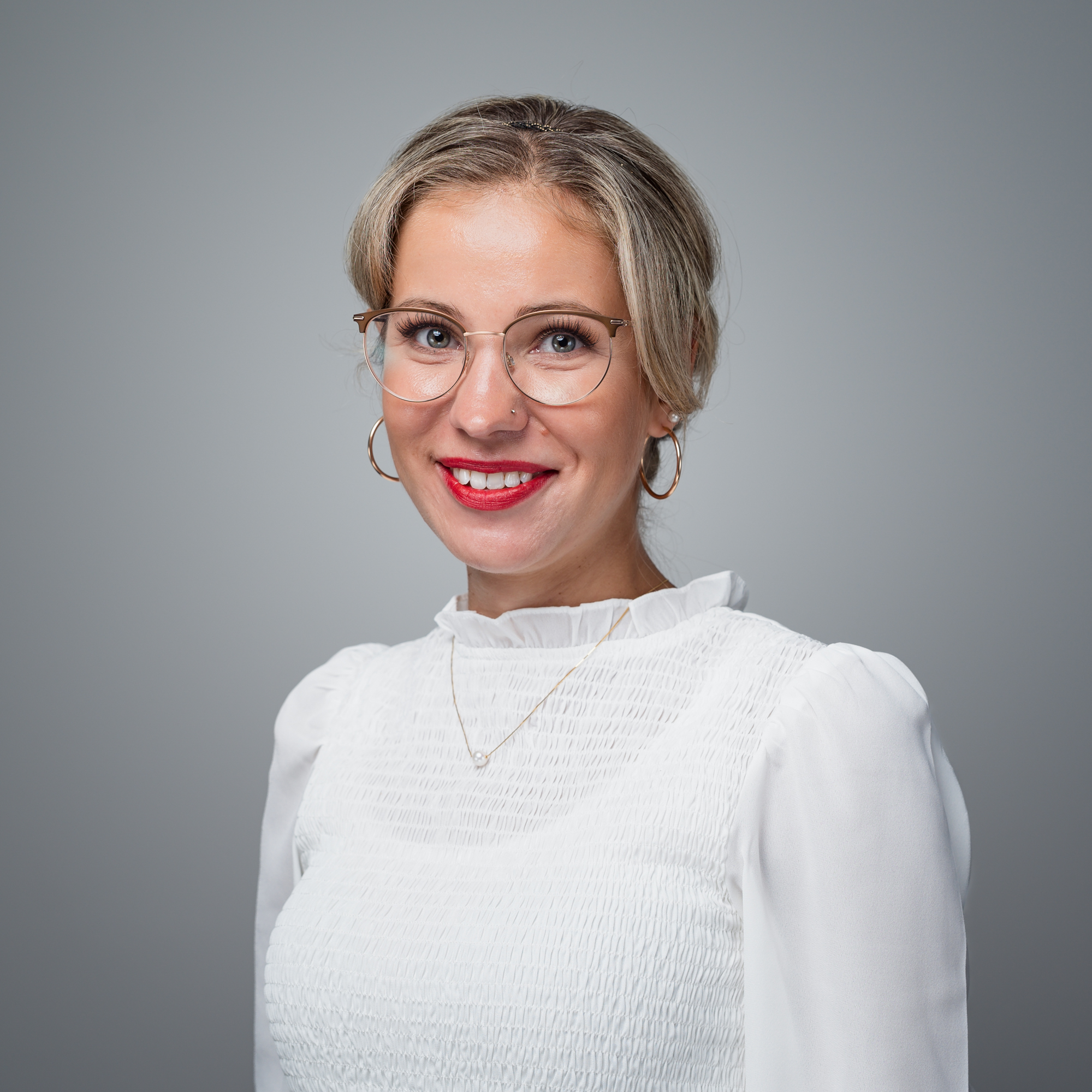 Porträt von Inna Einik, einer lächelnden jungen Frau mit blonden Haaren, Brille und rotem Lippenstift, die in die Kamera blickt.